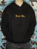 Person wearing a black hoodie with 'Beer Me.' text against a graffiti-covered wall.
