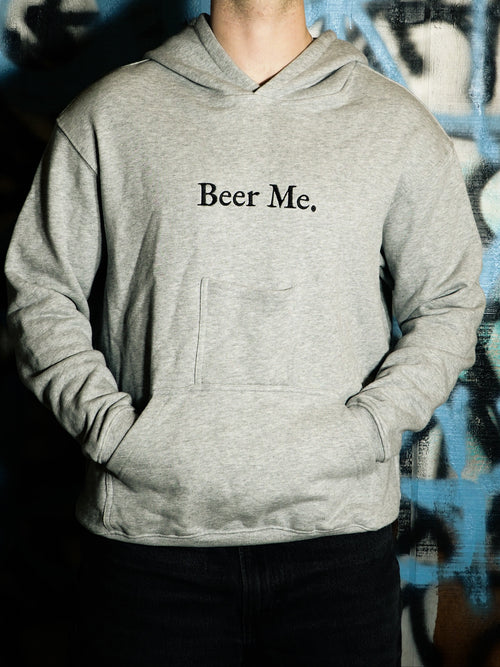 Person wearing a gray hoodie with 'Beer Me.' text against a graffiti-covered wall.