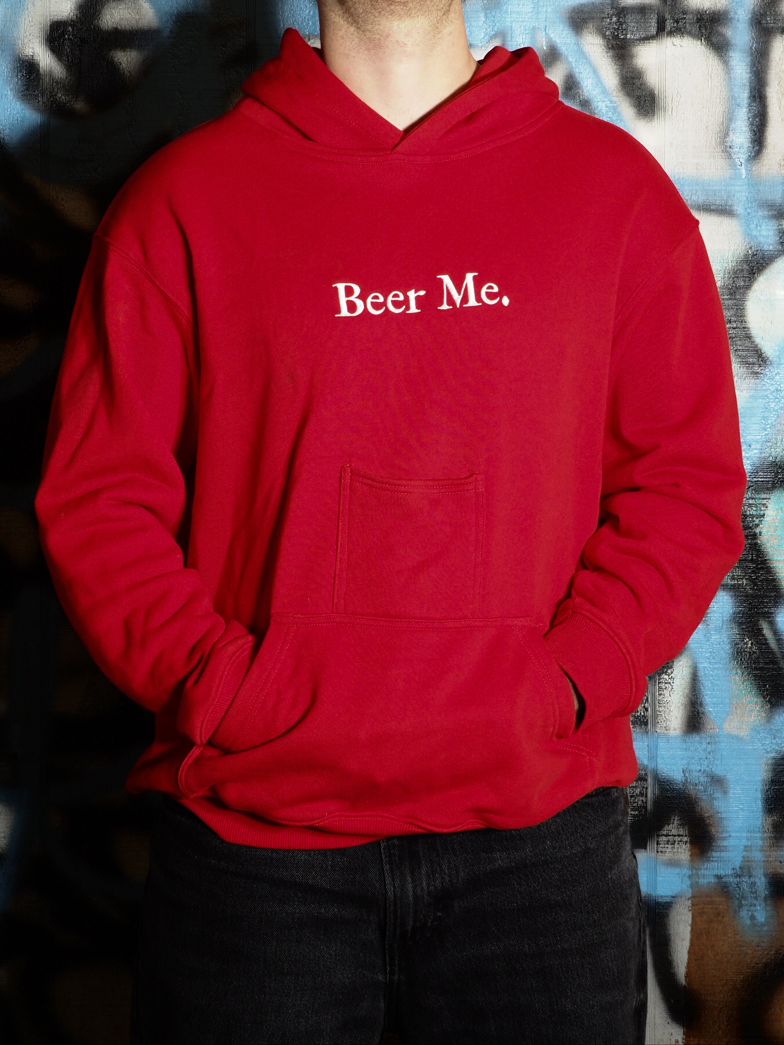 Person wearing a red hoodie with 'Beer Me.' text against a graffiti-covered wall.